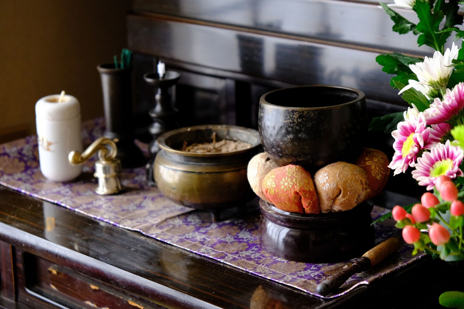 Bàn thờ Phật (butsudan) của gia đình bày cho dịp Obon — chuông orin trên đệm gấm cùng cây dùi gõ, lư hương đồng thau, nến trắng, hoa cúc và những quả hypericum đỏ, trên tấm vải tím ánh vàng.
