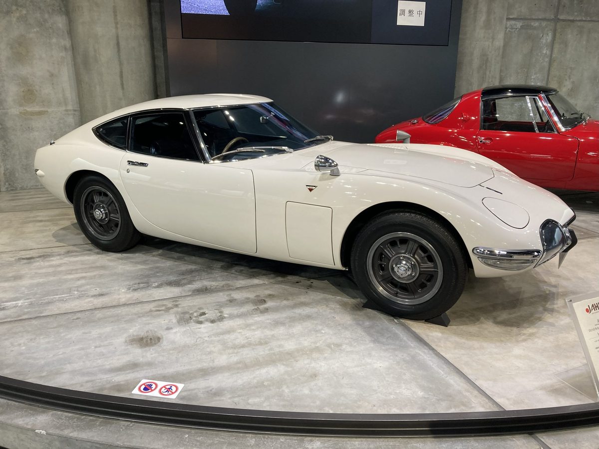 The elegant white Toyota 2000GT on its turntable, a red sports car waiting just behind.